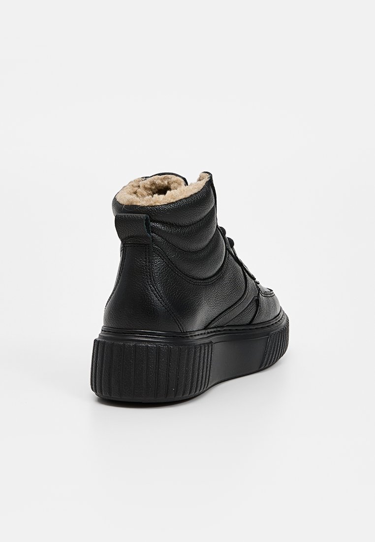 Czarne skórzane sneakersy za kostkę z miękkim beżowym wyściółką, teksturowaną górą, miękkim kołnierzem i grubą czarną kauczukową podeszwą. Brak widocznego logo.