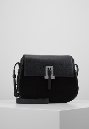 Schwarze Umhängetasche aus Leder und Wildleder mit silberner Schnallenverschlussschnalle und verstellbarem Riemen, präsentiert auf einem weißen Podest vor schlichtem grauem Hintergrund.