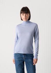 Light blue turtleneck sweater in soft fabric with long sleeves, fitted at the neck, paired with casual blue jeans.