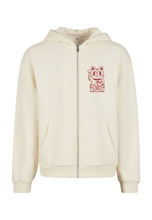 Kremowa bluza rozpinana z miękkiego materiału. Posiada grafikę czerwonego kota na lewej piersi oraz kieszenie z przodu, a także ściągacze na mankietach i u dołu.