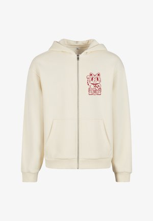 Kremowa bluza rozpinana z miękkiego materiału. Posiada grafikę czerwonego kota na lewej piersi oraz kieszenie z przodu, a także ściągacze na mankietach i u dołu.