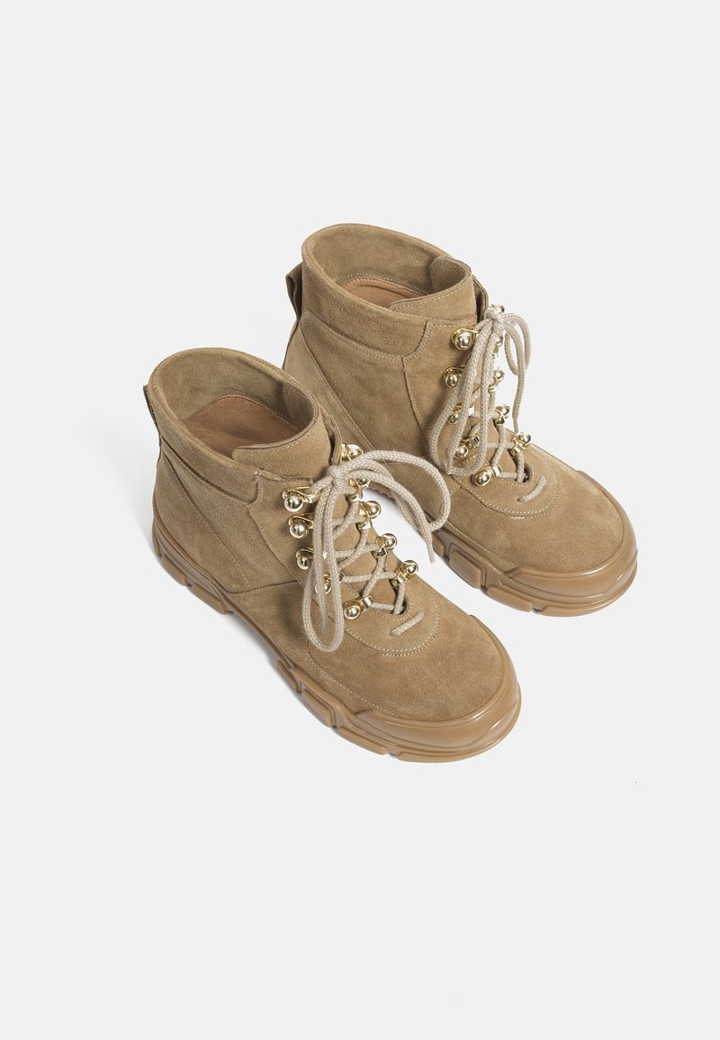Bottes montantes en daim couleur tan avec une finition texturée, dotées de ferrures dorées, de lacets ronds et d'une semelle épaisse en caoutchouc.
