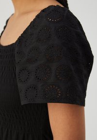 Μαύρο φόρεμα με υφή και κοντά μανίκια, διακοσμημένα με περίπλοκες κυκλικές κεντημένες λεπτομέρειες. Τα μανίκια διαθέτουν κοψίματα.