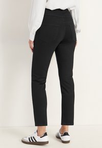 Svarta jeans i denim med hög midja, smal passform och två bakfickor, i kombination med vita sneakers med svarta ränder.