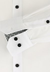 Weißes Hemd mit schwarzen Knöpfen, spitzem Kragen und strukturierten grauen Details auf dem inneren Kragen. Knitterfreier Stoff und strukturierter Schnitt.