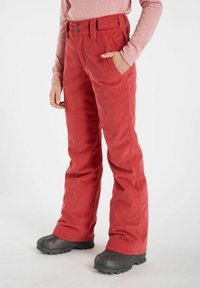 Rote Cord-Hosen mit geradem Schnitt, ausgestattet mit zwei Fronttaschen und zwei Knopfverschlüssen. Kombiniert mit grauen, strukturierten Stiefeln.