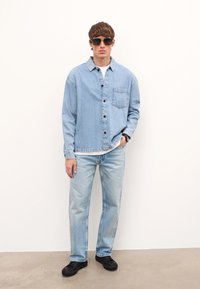 Heleheline teksajakk eesmine taskuga, nööpide sulgemisega, kantud valge särk üle. Koos helehelesiniste teksade ja mustade spordikennaritega.