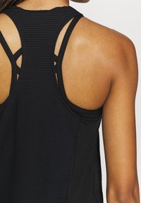 Bakifrån av en person som bär en svart texturerad racerback-linne som visar hudtonen på axlarna och övre delen av ryggen.