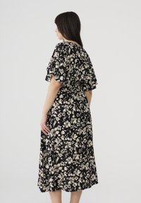 Abito con stampa floreale su sfondo nero e fiori bianchi. Presenta maniche a sbuffo corte e una vita aderente, raggiungendo la lunghezza a metà polpaccio.