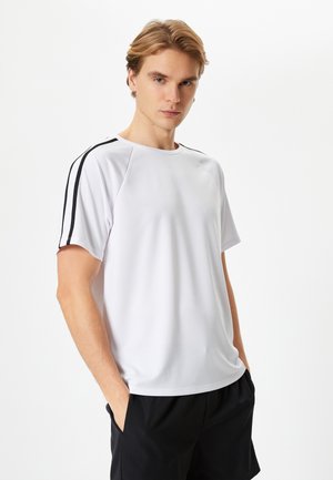 Hvid atletisk T-shirt med sorte sidelister, lavet af glat stof, med rund halsudskæring og korte ærmer, båret med sorte shorts.