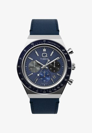 Ceasul cronograf Timex Q are un cadran albastru, hardware argintiu, un bezel tachimetric și o brățară din piele maro închis. Subcadranele sunt negre și albastre.
