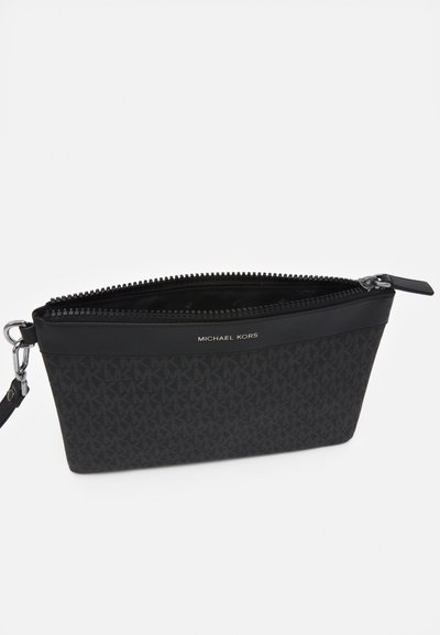 Pochette bracelet noire Michael Kors avec motif monogramme, ouverture zippée et bandoulière amovible sur fond blanc.