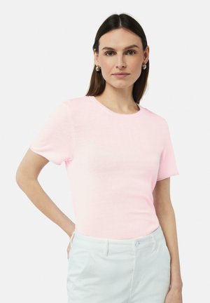 Lichtroze T-shirt met korte mouwen en een ronde halslijn, gemaakt van zachte stof. Model draagt lichtgekleurde broek en poseert met de handen op de heupen.