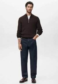 Donkerbruine ribgebreide trui met een ritskraag, gecombineerd met donkerblauwe denim broek en zwarte instappers, die een klassieke pasvorm en gestructureerde materialen laat zien.