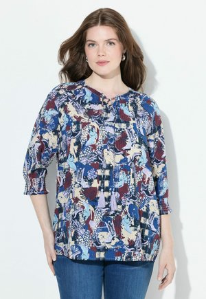 Blusa multicolore con un motivo floreale e astratto, scollatura rotonda con fiocco, maniche a 3/4 e dettagli a nappina. Tessuto leggero, vestibilità comoda.