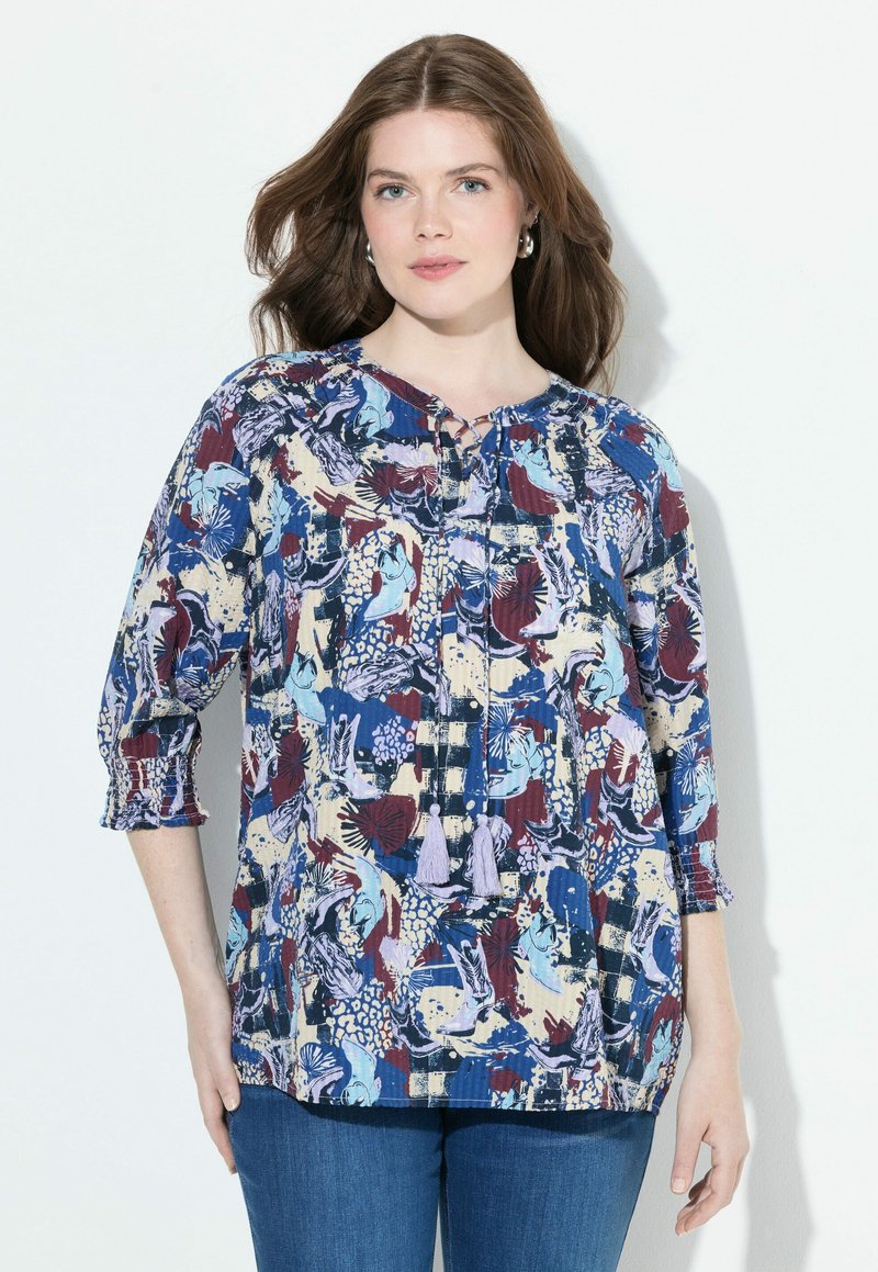 Bunt gemusterte Bluse mit floralen und abstrakten Motiven, runder Halsauschnitt mit Bindeband, 3/4-Ärmel und Fransenakzente. Leichtes Material, lockere Passform.