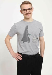 Gray cotton t-shirt featuring a printed design of a character in a cape walking a small robot. Simple shape with short sleeves.