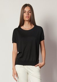 Svart kortärmad topp med rund halsringning och avslappnad passform. Tillverkad av mjukt material, med ribbat nederkant och subtil lyster.