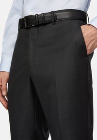 Černé kalhoty s hladkým povrchem, přizpůsobeným střihem a jemným leskem. Černý kožený opasek se nachází na pase, s kovovou sponou.