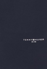 Camiseta azul marino con textura acanalada, que presenta la marca blanca "TOMMY HILFIGER EST. 1985" en la parte baja delantera. Diseño clásico con cuello redondo.
