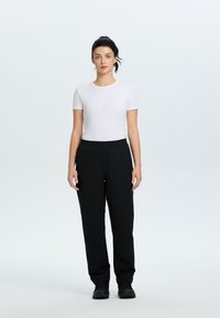 Witte shirt met korte mouwen en zwarte elastische broek. De outfit heeft een eenvoudig design met een gladde textuur. Zwarte schoenen maken de look af.