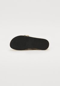 Suola in gomma nera con texture ondulata, caratterizzata da un materiale superiore intrecciato di un beige chiaro. Nessun marchio visibile o elementi di design distintivi.