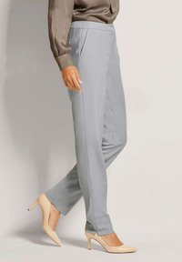 Lichtgrijze op maat gemaakte broek met een gladde textuur, voorzien van voorplooien en een slim fit, gecombineerd met beige hoge hakken.