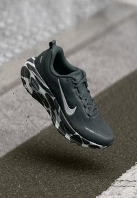 Sivé bežecké topánky s textúrovaným sieťovaným zvrškom, s bielym logom swoosh a charakteristickou čierno-bielou vzorovanou podrážkou.