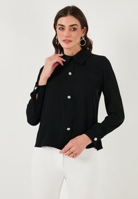 Black button-up blouse with long sleeves, a collar, decorative silver buttons, and a relaxed fit, made from smooth, lightweight fabric.