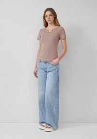 Lichtroze, getailleerde top met korte mouwen en een V-hals, van textuurstof. Gepaard met lichtblauwe jeans met hoge taille en brede pijpen, en witte platform schoenen.
