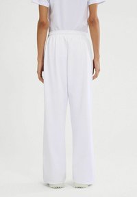 Pantalones anchos blancos con cintura elástica, que cuentan con una textura suave y un corte holgado, combinados con zapatillas ligeras.