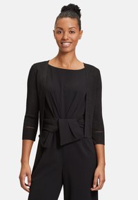 Fekete kardigán, háromnegyedes ujjakkal, enyhén texturált anyagból, nyitott elülső kialakítással és apró kivágásokkal a mandzsetták közelében.