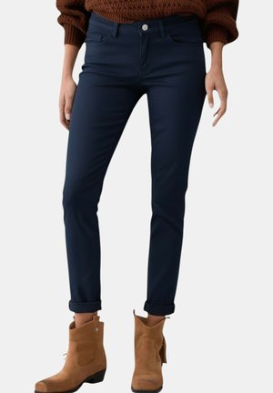 Gambe con jeans slim blu scuro risvoltati alle caviglie, abbinati a stivaletti in suede color tabacco con tacco basso e maglione marrone.