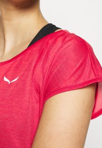 Fuksia lyhythihainen urheilupaita, jossa on pehmeä ja teksturoitu kangas. Alla musta hihna. Valkoinen logo edessä.