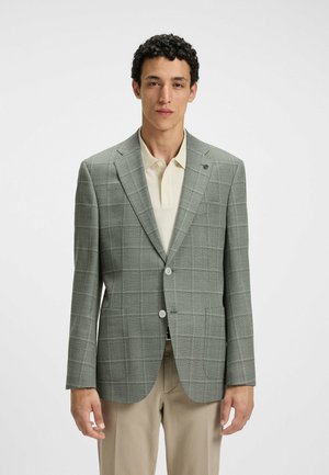 Grau kariertes Blazer aus strukturiertem Stoff, mit zwei Knöpfen, abgesetzten Revers und seitlichen Taschen, getragen über einem hellbeigen Poloshirt.