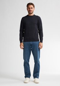 Granatowy sweter z okrągłym dekoltem uszyty z miękkiego materiału, w połączeniu z jasnoniebieskimi dżinsami. Stylizacja dopełniona białymi sneakersami. Prosty i swobodny design.