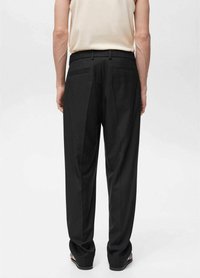 Pantalones negros, ajustados y de corte recto, con dos bolsillos traseros, pliegues y una textura de tela suave. Combinados con una blusa de color claro.