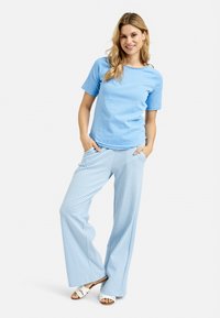 Light blue short-sleeve t-shirt paired with loose, striped wide-leg pants in light blue and white. Model wearing white sandals.