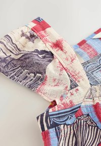 Gros plan d'une manche en tissu coloré avec un détail froncé et un motif imprimé en tons rouge, bleu, marine et crème.