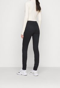Jeans ajustados negros de cintura alta con una textura suave, que presentan un diseño clásico de cinco bolsillos y bolsillos traseros cosidos. Combinados con zapatillas blancas.
