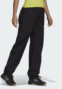 Pantaloni sportivi neri con vestibilità ampia, tessuto leggero e tasche con cerniera. Indossati con scarpe sportive nere con accenti grigi.