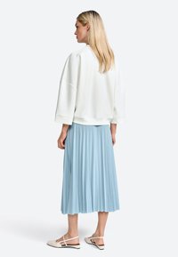 Hvid, oversized sweatshirt med brede ærmer parret med en plysskjorte i lys blå og beige slingback flade sko, vist fra bagsiden.