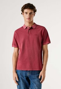 Camiseta polo de algodón roja con cuello clásico, tapeta con dos botones y mangas cortas. Presenta un discreto bordado de la marca en el pecho.
