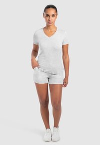 Grijs T-shirt met korte mouwen en V-hals, gecombineerd met bijpassende korte broek, beide gemaakt van zachte, lichte stof. Model draagt witte sneakers.