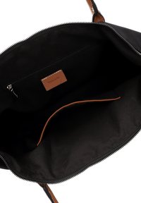 Interno in tessuto nero di una borsa, con un'etichetta in pelle marrone e una tasca con zip. La forma è rettangolare con lati morbidi e una sola tracolla.
