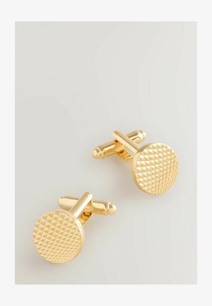 Pár okrúhlych zlatých manžetových gombíkov s textúrovaným pyramídovým vzorom na čelách, ležiacich na svetlošedej ploche.