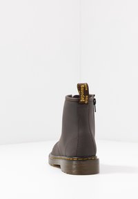 Brązowe botki za kostkę z teksturowanym wykończeniem, elastycznymi bokami, tylną pętlą do ciągnięcia oraz masywną podeszwą z żółtym przeszyciem.