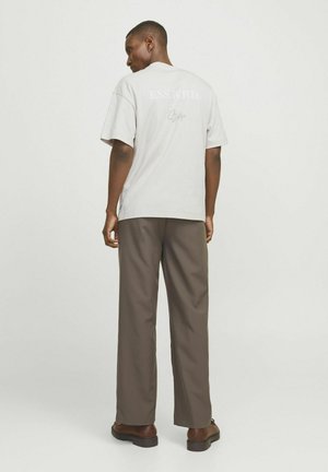Camiseta de algodón gris con el texto "ESS.WRD." en la parte posterior. Combinada con pantalones de pierna ancha marrones y zapatos oscuros, presenta un ajuste relajado.