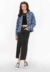 Blå denimrutig jacka över en svart kort topp, tillsammans med en svart maxikjol med en framskjutning och svarta sneakers med vita sulor.