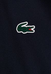 Zielony krokodyl z czerwonym pyskiem obrysowanym na biało na ciemnoniebieskim teksturowanym tle.